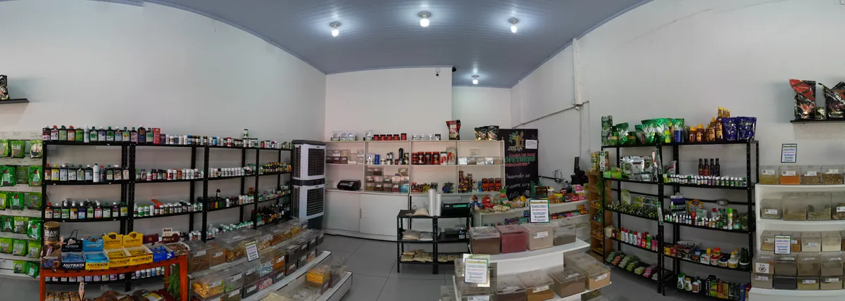 Vista panorâmica do interior da loja, com a parede de ervas, prateleiras de suplementos e o granel